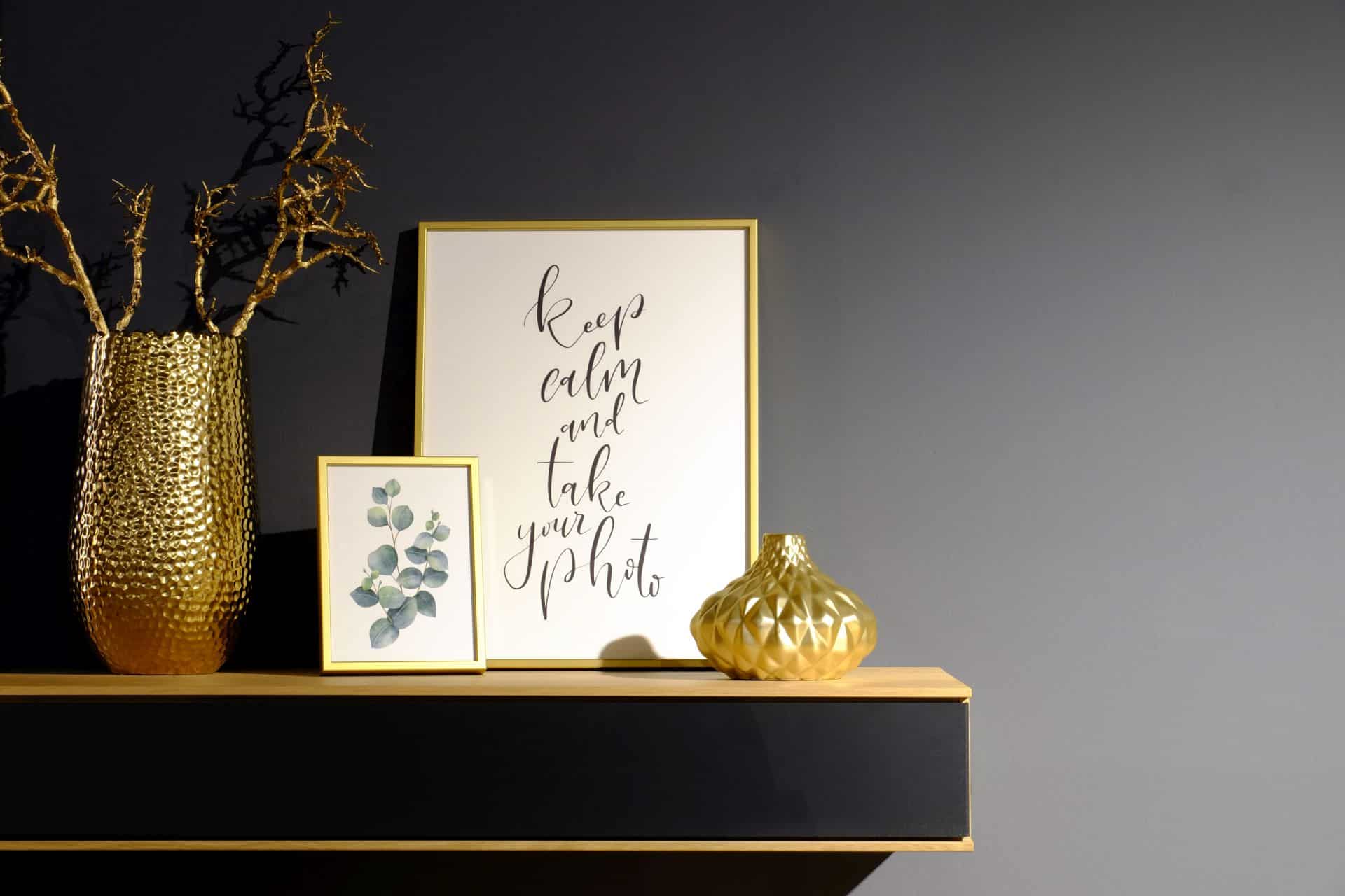 Gold-Edition-Wohnambiente Rahmen auf einem ebenfalls goldenen Sideboard neben einer goldenen Vase mit vergoldetem Ast darin