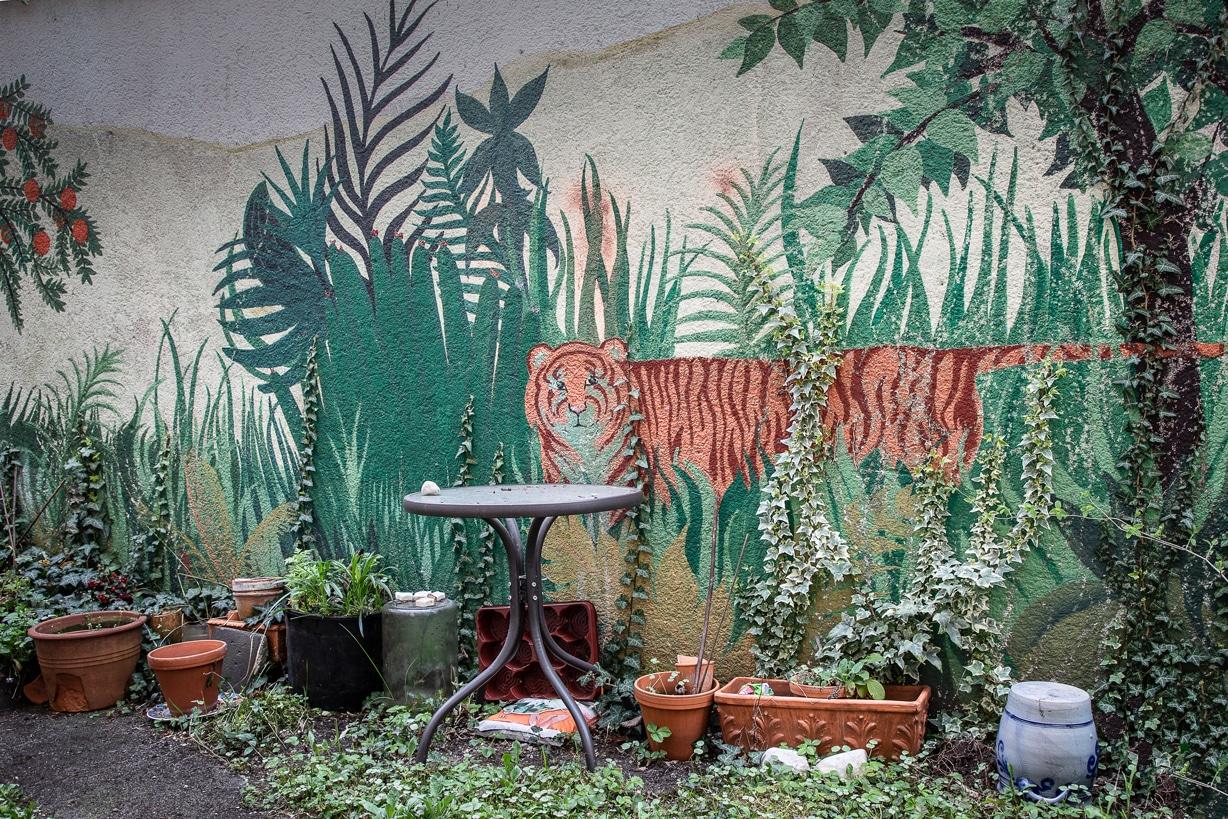 Ein Innenhof mit einem Tigergraffiti. Davor stehen zahlreiche Pflanzer sowie ein Stehtisch