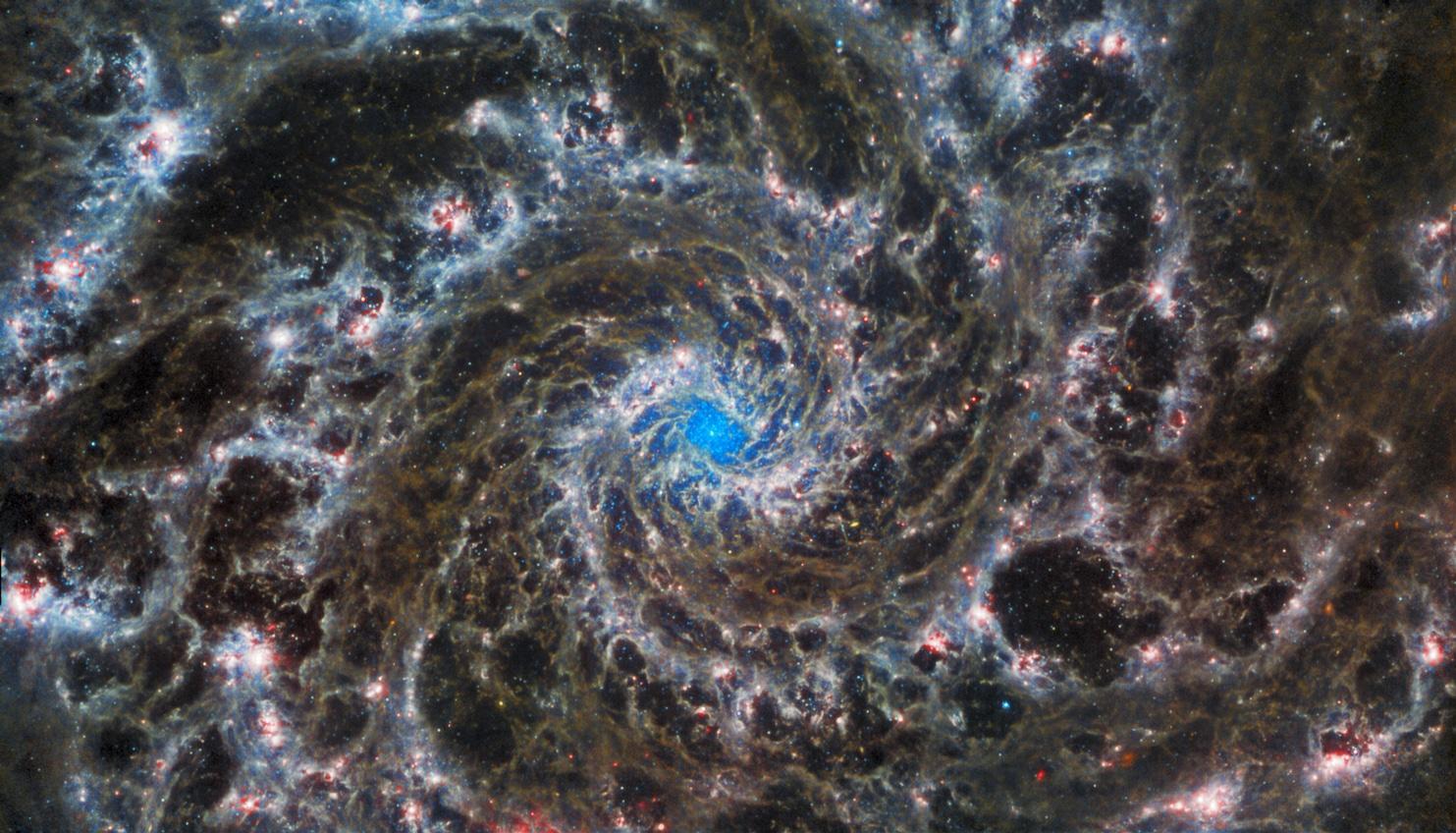 Die Spiral-Galaxie M74, auch Phantom-Galaxie genannt. M74 befindet sich 32 Millionen Lichtjahre von der Erde entfernt im Sternbild der Fische. Neben den feinen Filamenten aus Staub und Gas, die Teile der eindrucksvollen Spiralarme ausmachen, sieht man im Zentrum einen Sternhaufen besonders junger Sterne. Mit der MIRI-Kamera kann das James-Webb- Teleskop im Infraroten die Sternentstehung, Alter und Massen der Sternhaufen genauestens vermessen.